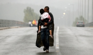 A Syrian refugee kisses his daughter as he walks through a rainstorm towards Greece's border with Macedonia, near the Greek village of Idomeni, September 10, 2015. Most of the people flooding into Europe are refugees fleeing violence and persecution in their home countries who have a legal right to seek asylum, the United Nations said on Tuesday. REUTERS/Yannis Behrakis - RTSFW6
